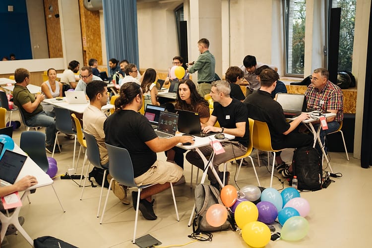 Teams working on laptops with collected balloons piled on the floor