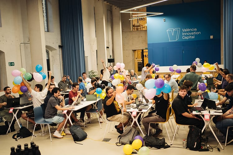 A hall full of participants raising balloons during the Valencia hackathon